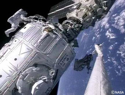 船外に出てザーリャ・ユニティ間の電源ケーブル結合作業をおこなう宇宙飛行士。手前に見えているのは、スペースシャトルからのびるロボットアーム。